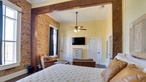 A bedroom with a large bed, a ceiling fan, a TV, and a brick wall. - Shop, Dine & Unwind at Historic Dtwn Marshall Apt (Marshall)