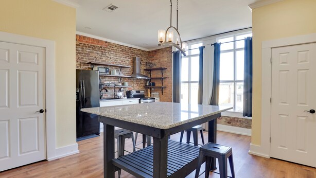 A kitchen with a granite countertop, black metal legs, and a hanging light fixture. - Shop, Dine & Unwind at Historic Dtwn Marshall Apt (Marshall)
