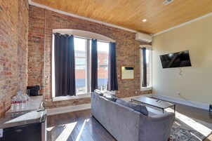 Una sala de estar con pared de ladrillo, un sofá, un televisor y una ventana con cortinas.