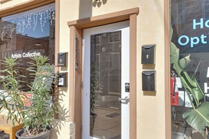 Entrada de un edificio con una puerta, un letrero que dice 'Artists Collective' y plantas en macetas.