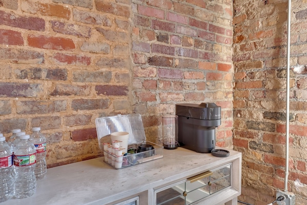 A brick wall with a white counter displaying water bottles, a coffee maker, and a tray with cups and containers. - Walk to Courthouse Sq! Loft-style Marshall Studio (Marshall)