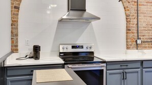 Une cuisine équipée d’une cuisinière en acier inoxydable, d’une machine à café et d’un mur en briques.