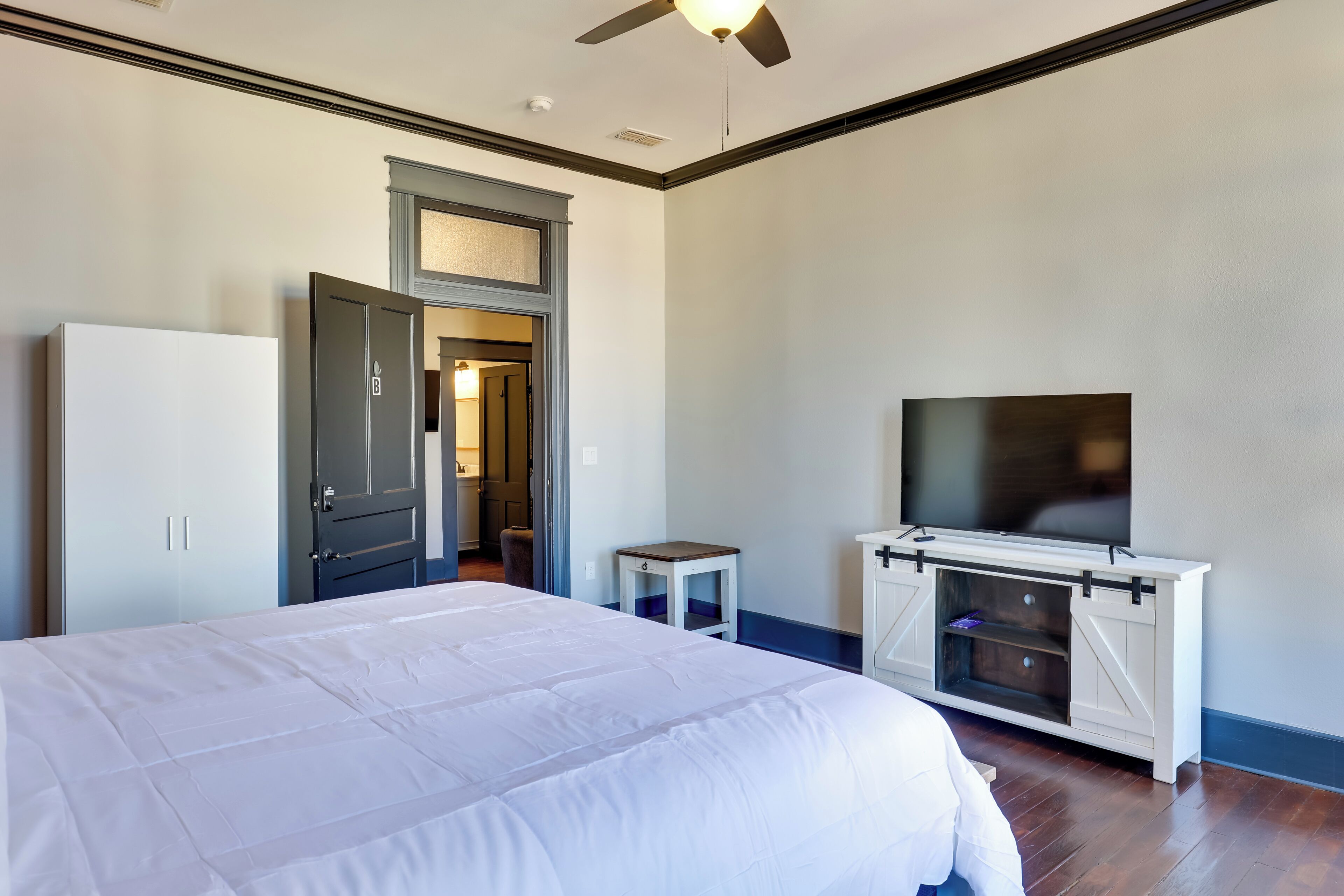 A bedroom with a large bed, a TV on a cabinet, and a door leading to another room.
