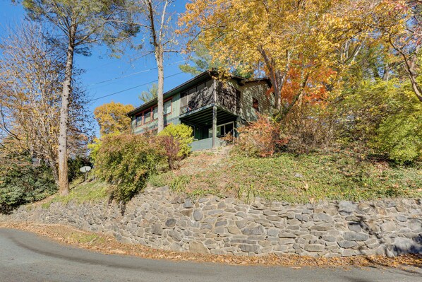 A two-story house with a stone retaining wall in front, surrounded by autumn foliage.