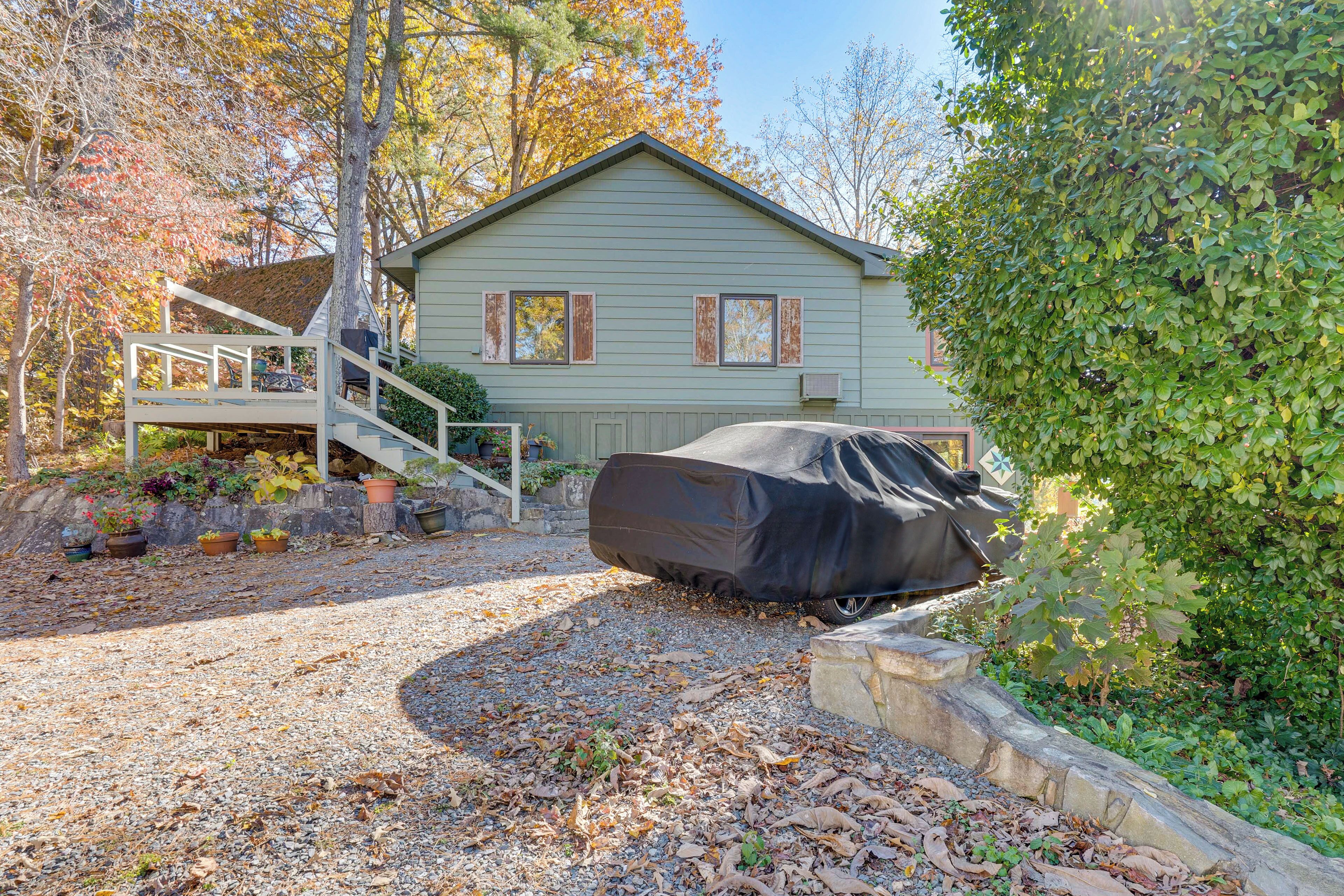 A two-story house with a covered car in the driveway, surrounded by trees and a gravel path.