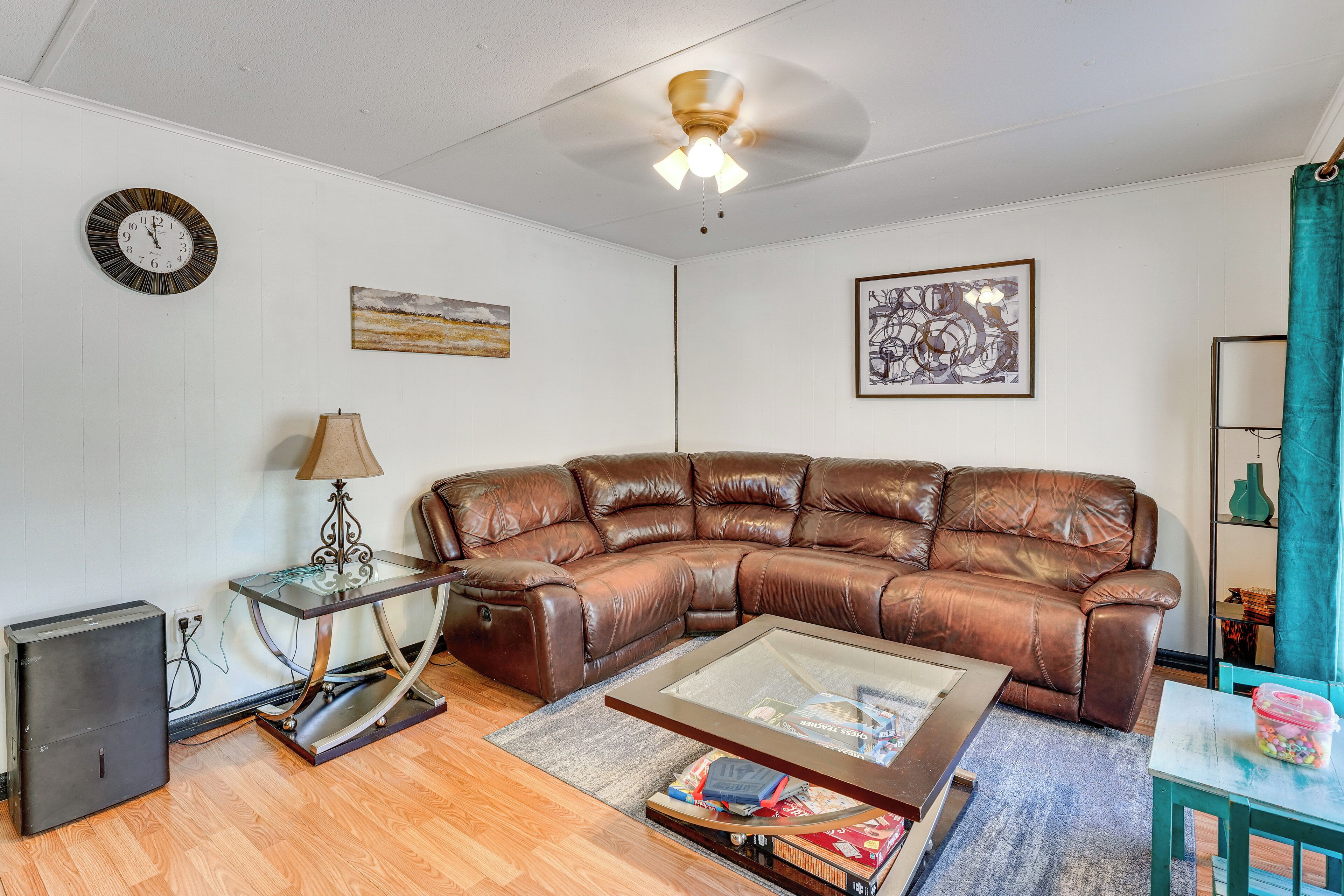 A living room with a leather sectional sofa, a glass coffee table, a lamp, a clock, and artwork on the walls.