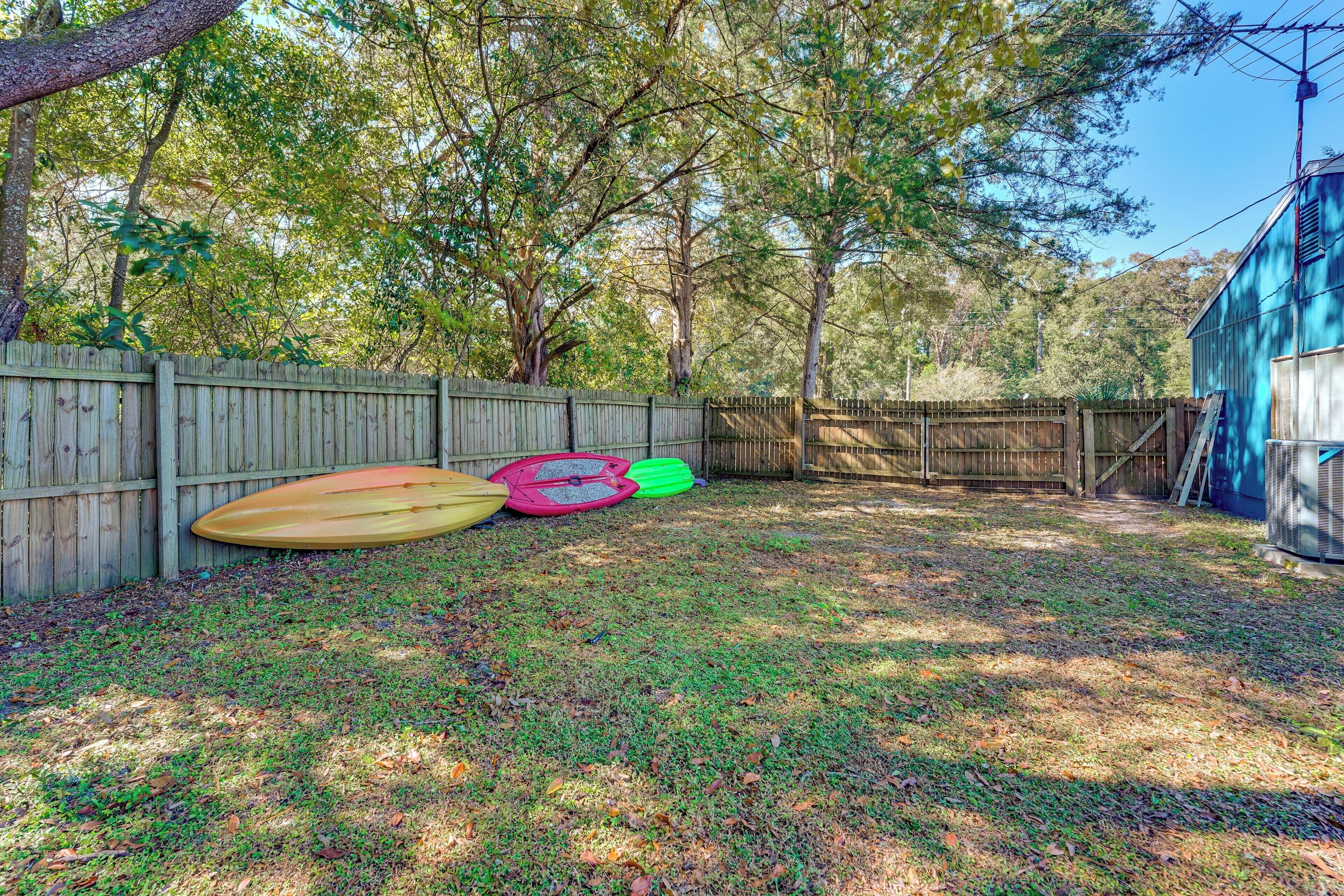 A fenced backyard with a wooden fence, a blue building, and three kayaks.