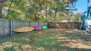 A fenced backyard with a wooden fence, a blue building, and three kayaks.