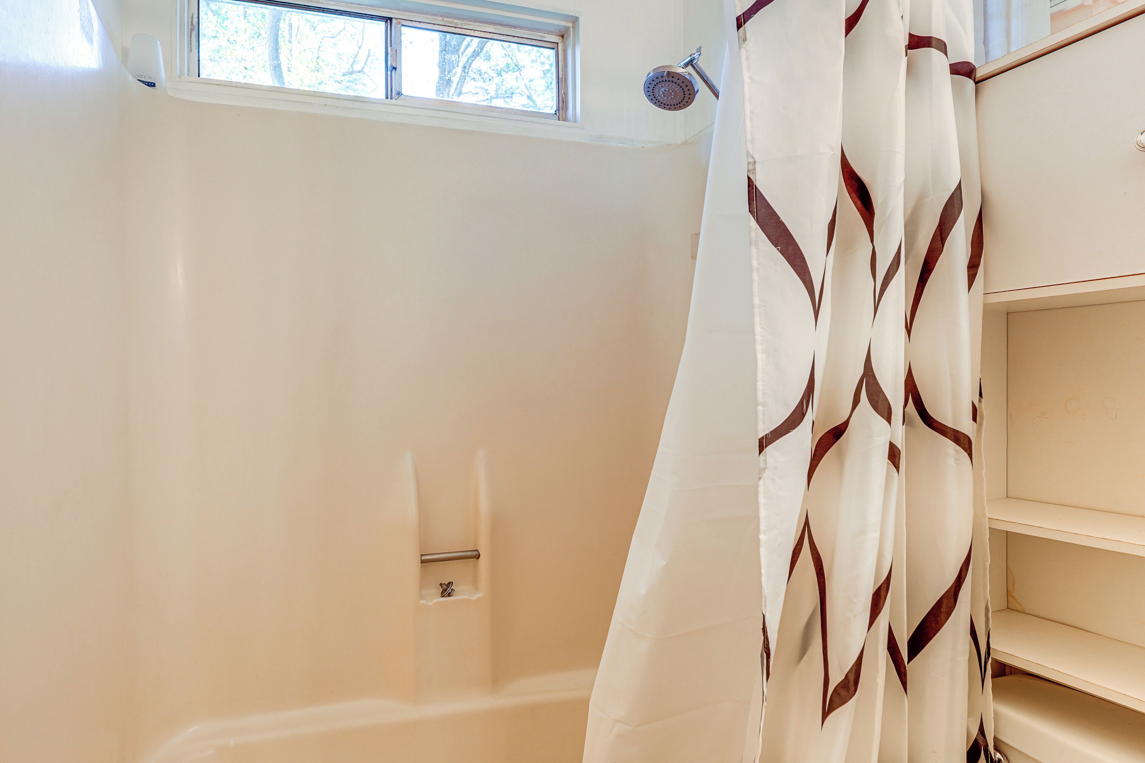 A bathroom with a shower, a window, and a white shower curtain with a geometric pattern.