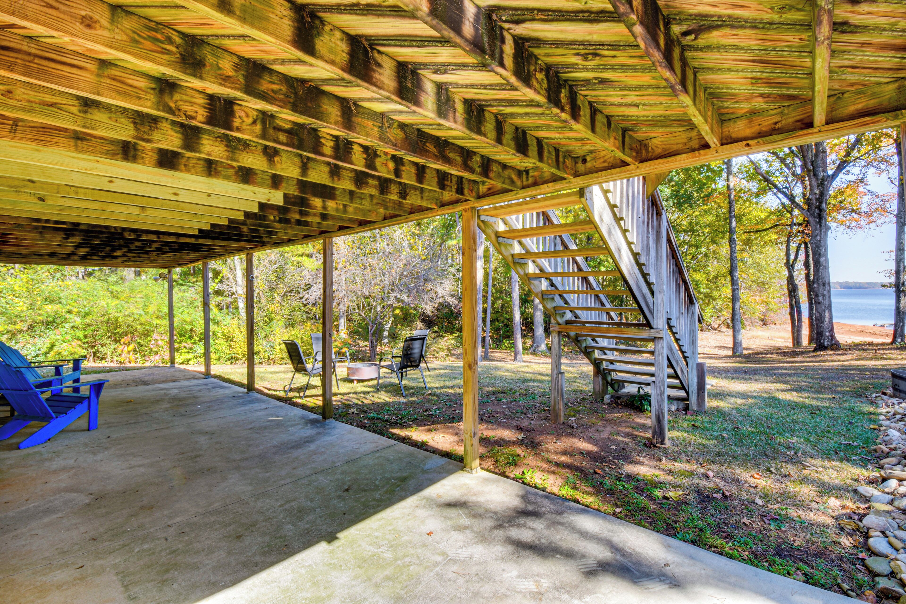 A covered outdoor area with a concrete floor, wooden beams, and a view of a lake.