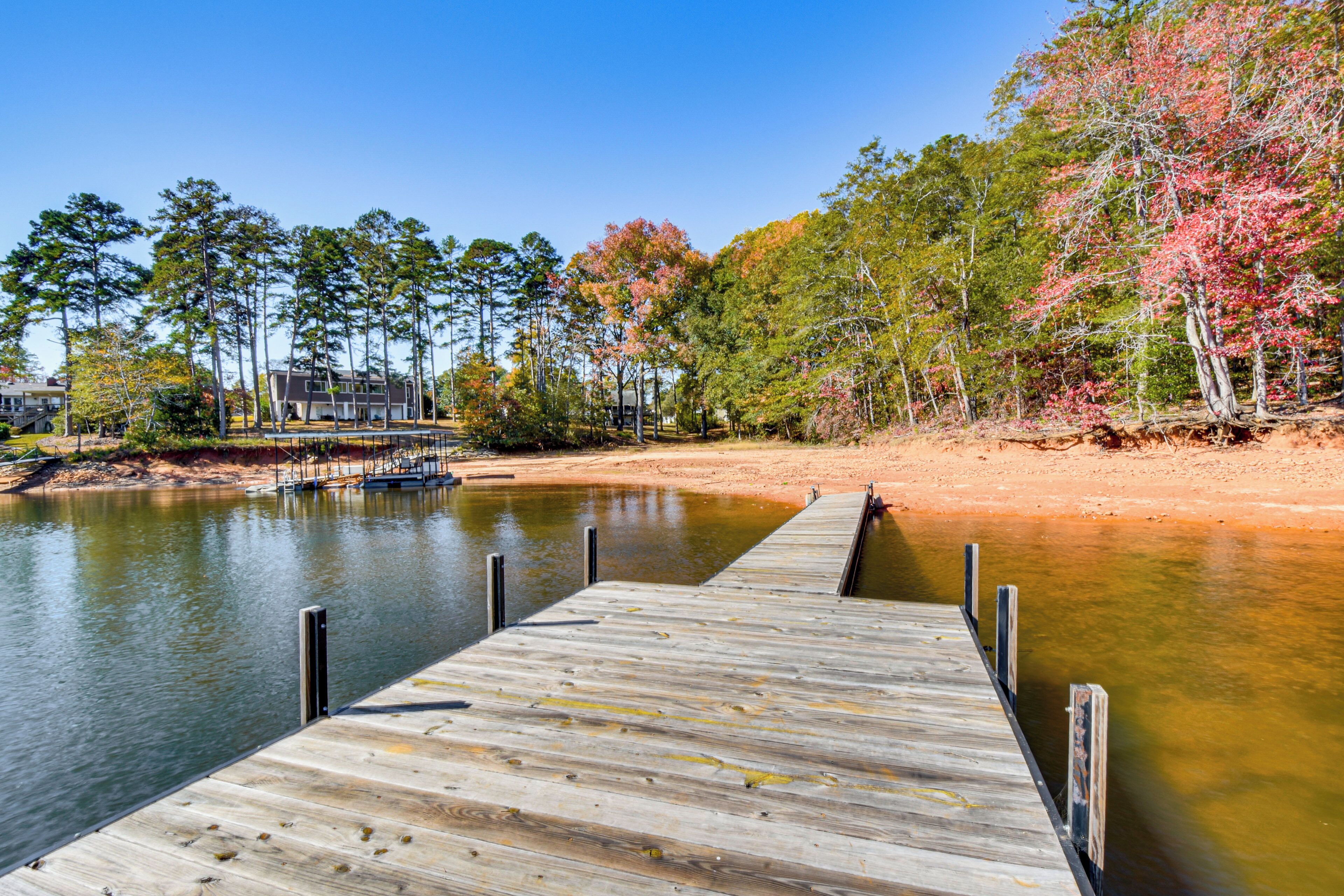A wooden dock extending into a calm lake with a backdrop of trees and a building.