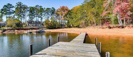 A wooden dock extending into a calm lake with a backdrop of trees and a building.