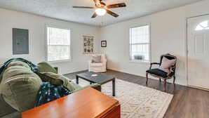 A living room with a ceiling fan, two windows, a white armchair, a black armchair, a wooden coffee table, and a green sofa. - 6 Mi to Mammoth Cave! Mtn-view Home w/ Fire Pit (Cave City)