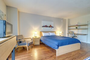 A modern hotel room with a wooden bed, a desk with a computer, a chair, and a small desk lamp. - Near Stadiums, Parks & Hospitals: Detroit Studio (Detroit)