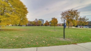 Ein Park mit Gras, Bäumen, einem Bürgersteig und einem Gebäude im Hintergrund.