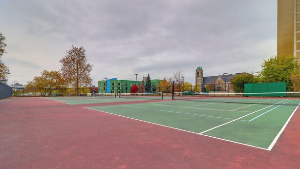 Ein Tennisplatz mit grünen und roten Belägen, umgeben von Bäumen und Gebäuden.