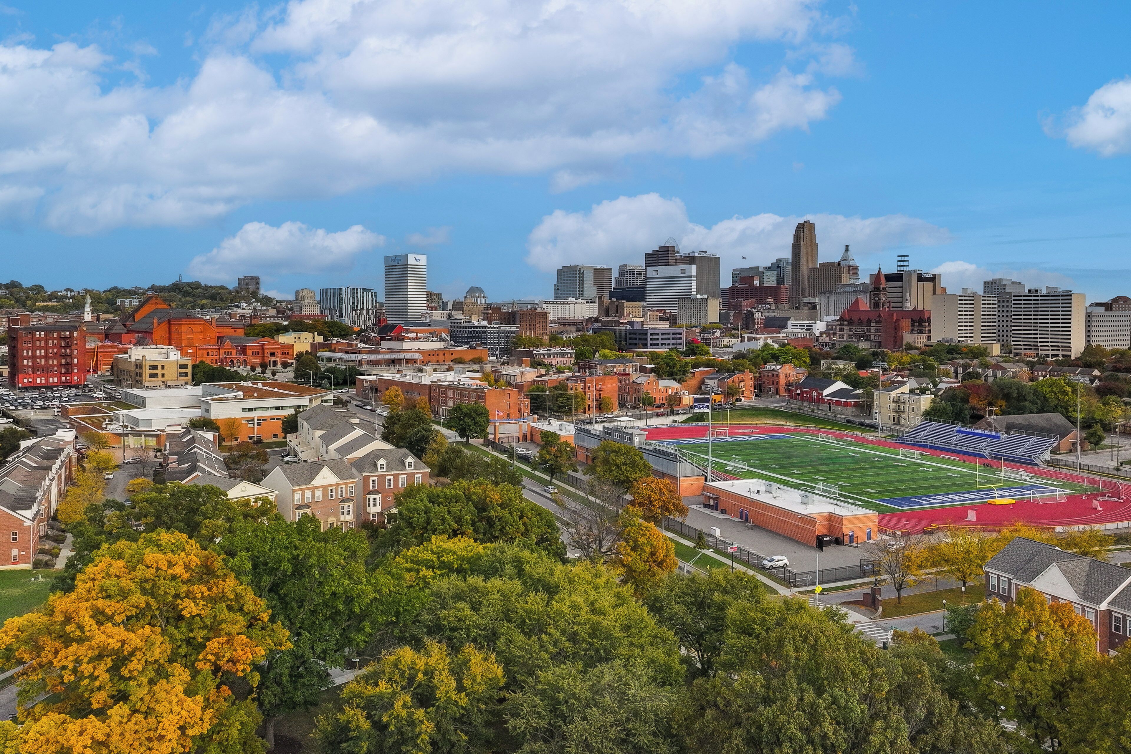 Panorama urbano con un campo sportivo in evidenza, diversi edifici e cielo sereno.