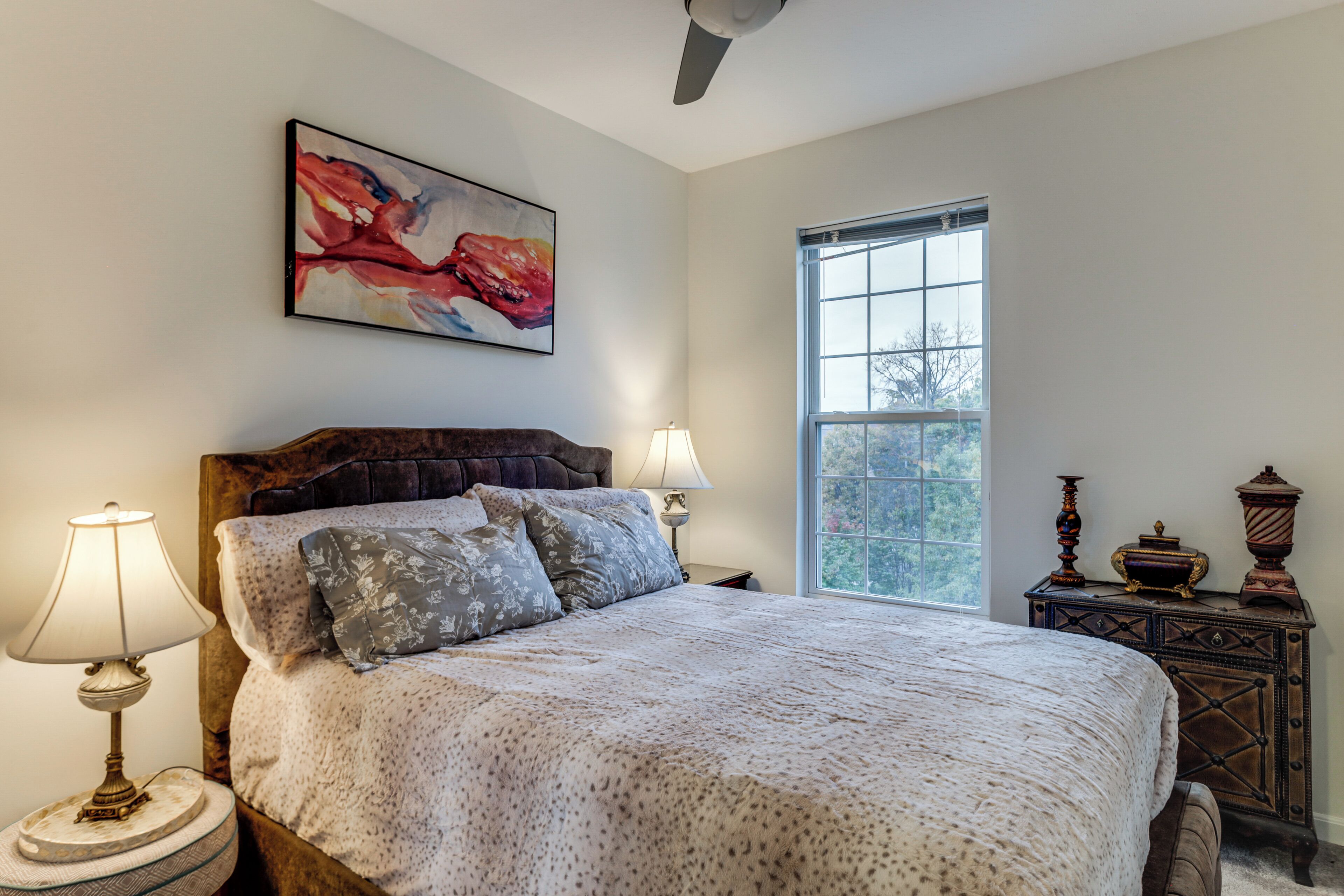A bedroom with a large bed, two bedside lamps, a window, and a decorative cabinet.