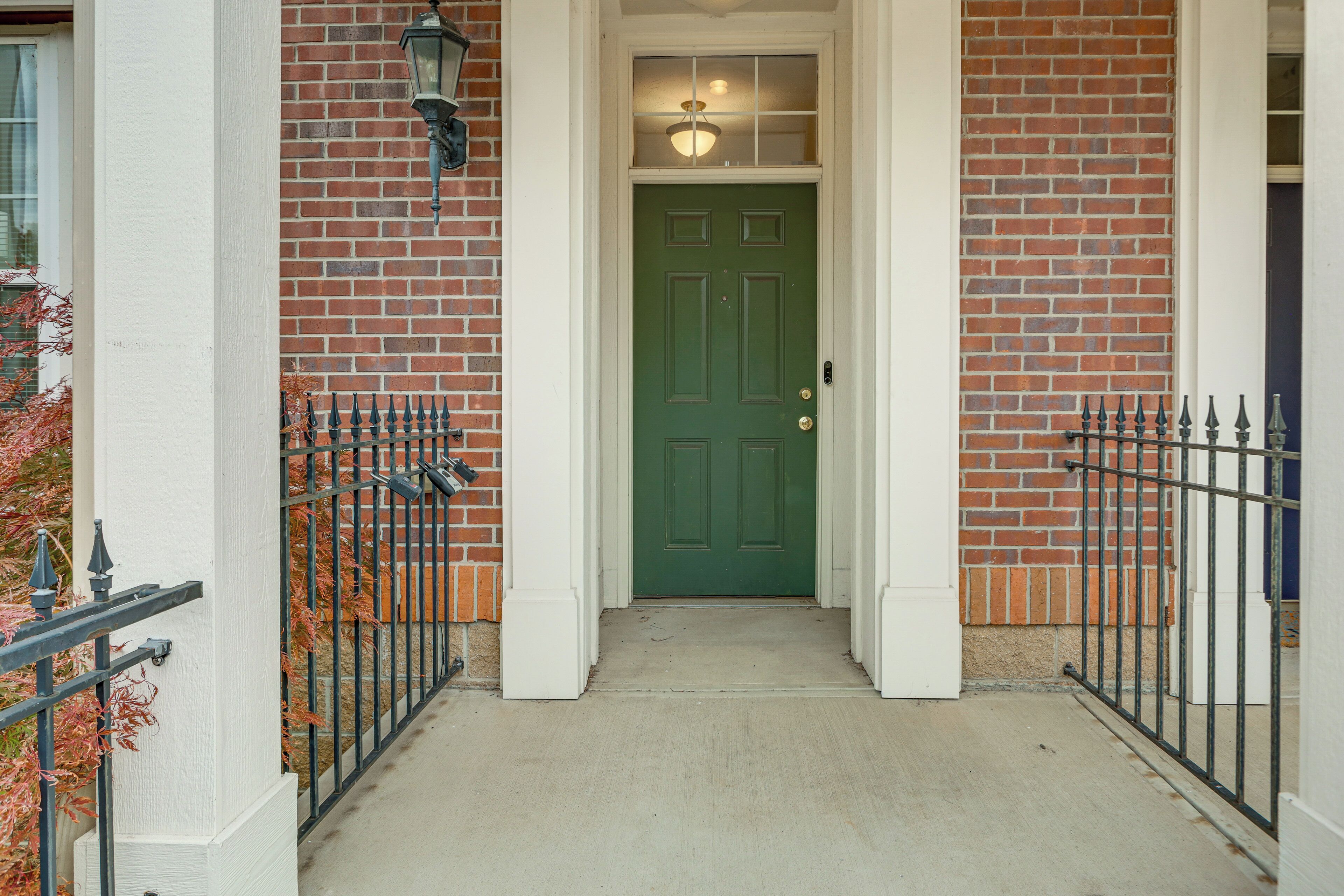 A green door with a white door frame, a brick wall, and a metal fence.