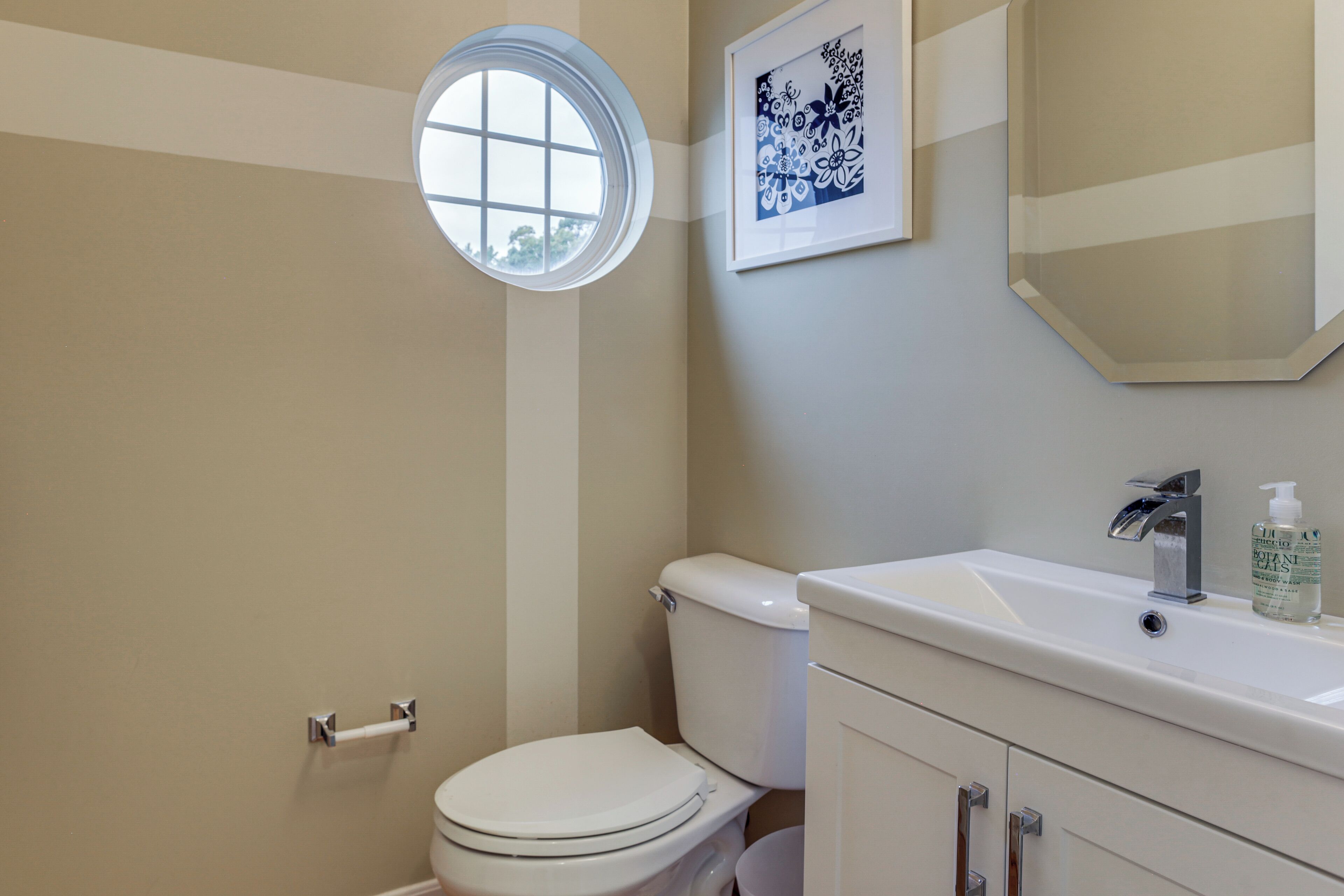 A bathroom with a toilet, a sink, a mirror, and a window.