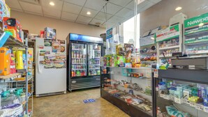 Una tienda de conveniencia con estantes llenos de diversos productos, un mostrador refrigerado y una sección de electrónica.