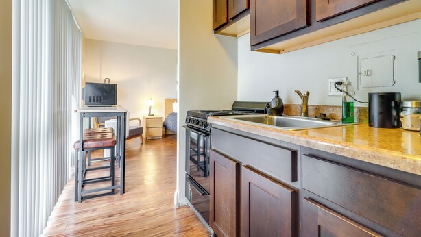 Una cocina moderna con armarios de madera, un lavamanos de acero inoxidable y un horno empotrado. Hay una pequeña zona de comedor con una mesa y sillas.