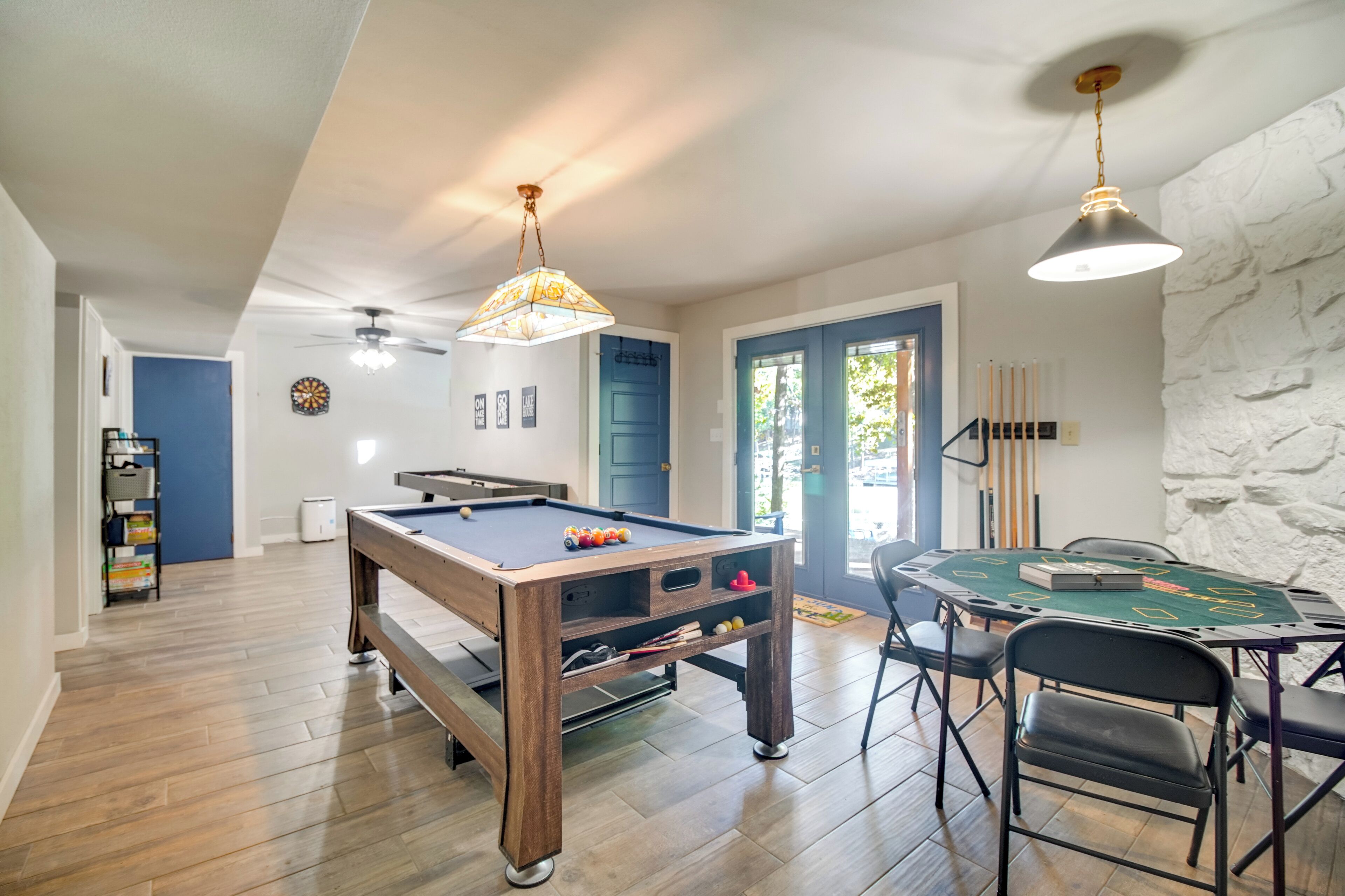 Een ruime kamer met een pooltafel, een blackjacktafel met groene doek en een plafondventilator.