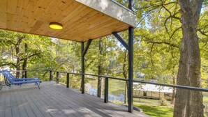 A wooden deck with a blue lounge chair, a metal railing, and a view of trees and a body of water. - Game Room, Dock & Hot Tub: Grand Lake Getaway (Afton)