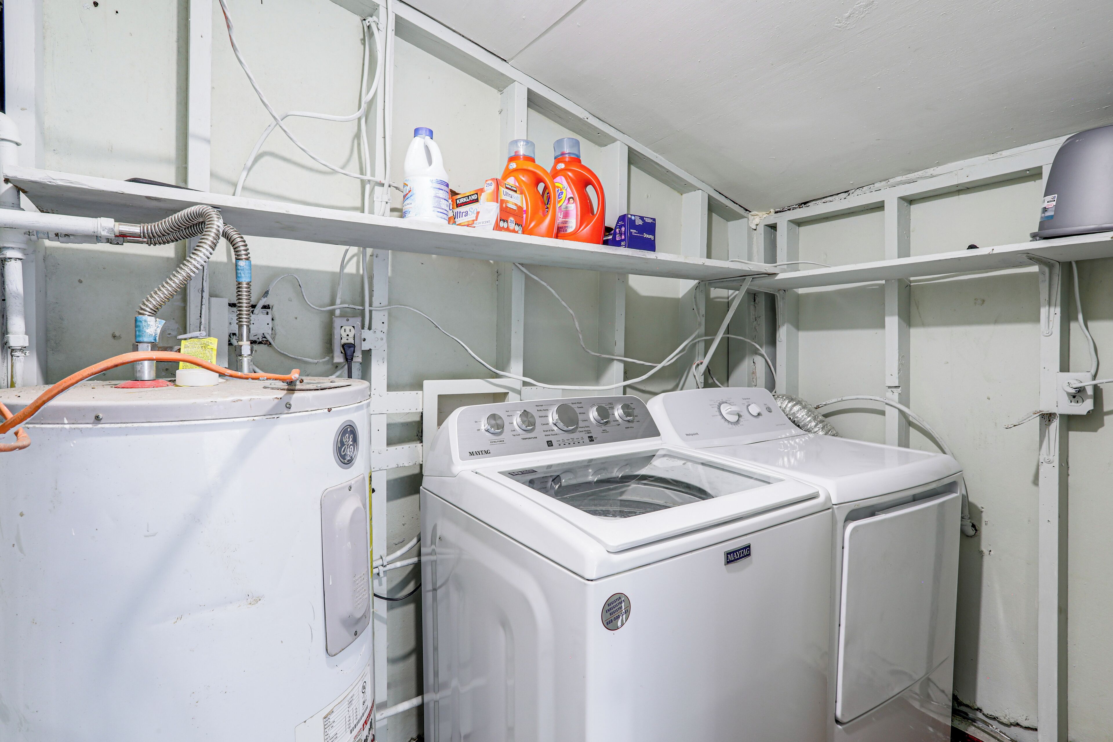 A laundry area with two washing machines, a shelf with detergent bottles, and visible plumbing.