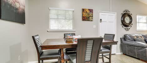 Un coin repas avec une table et des chaises en bois, un tableau au mur, une porte et une horloge.