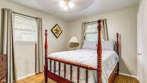 A bedroom with a four-poster bed, a dresser, a nightstand, a lamp, and a window with curtains.