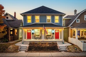 A two-story house with a porch, a flag, and a small garden. - 3 Mi to Dtwn Indy: Urban Retreat w/ Outdoor Space (Indianapolis)