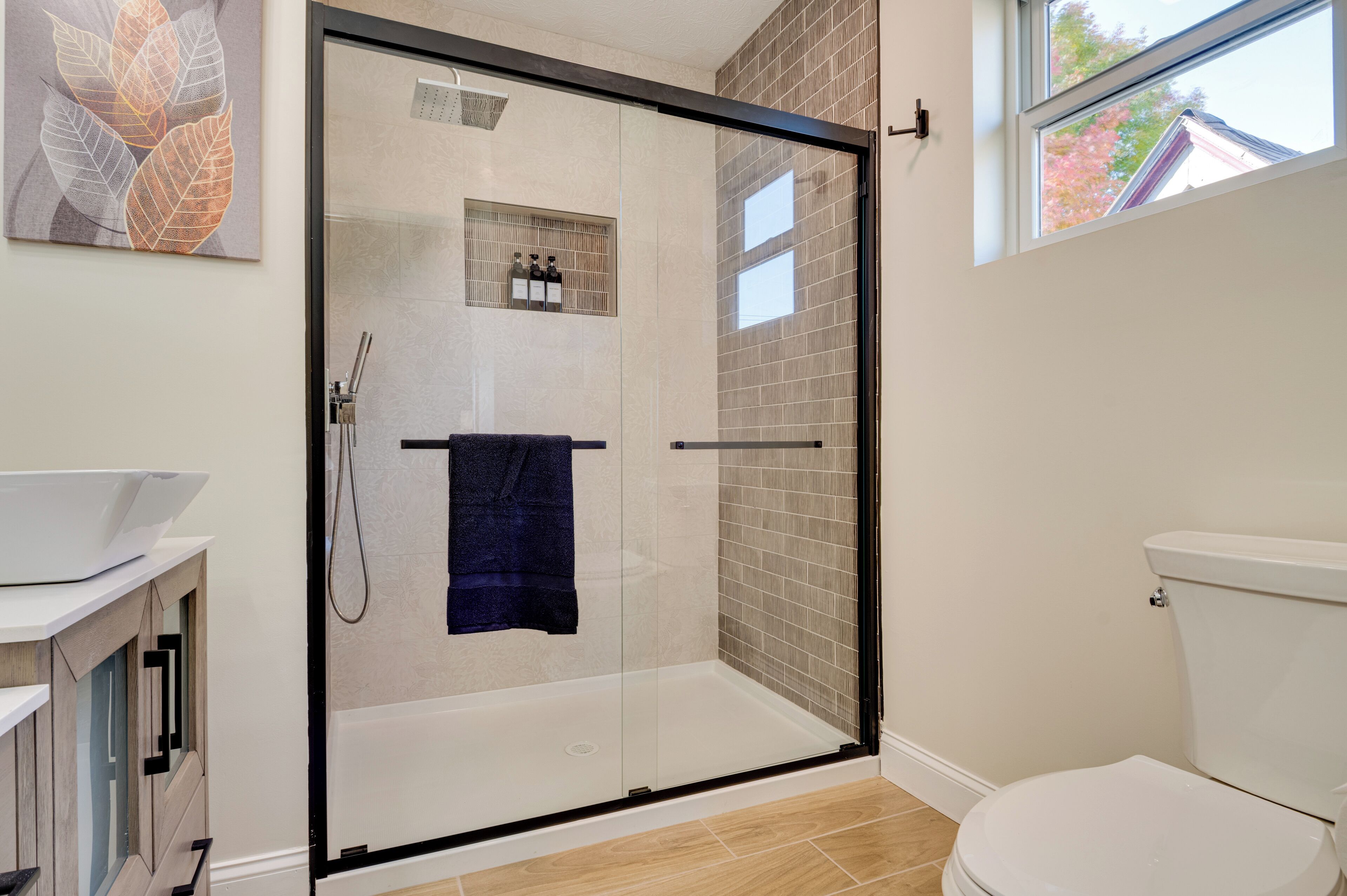 Et moderne badeværelse med et glasafskærmet brusebad, toilet og en vask med skab.