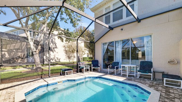 A swimming pool with a glass enclosure, surrounded by outdoor furniture and a covered patio area. - 5 Mi to Disney Parks: Family Home w/ Resort Perks! (Kissimmee)