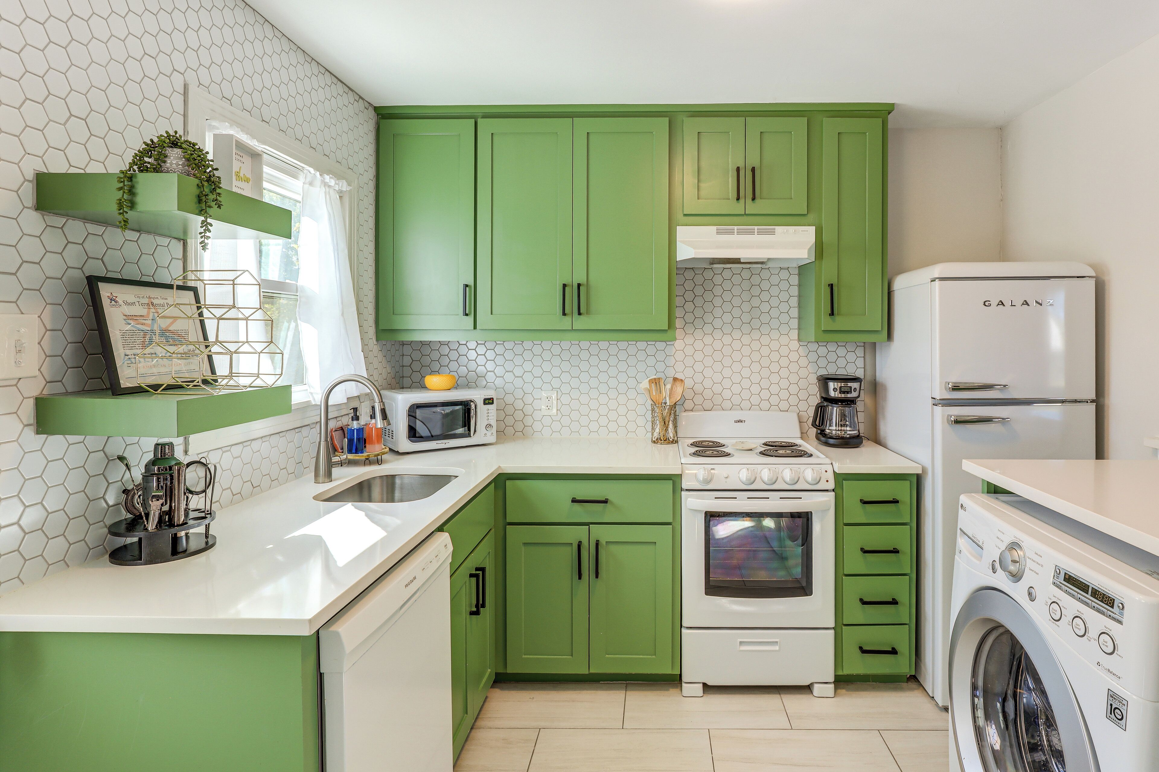 Une cuisine avec des meubles de couleur verte, un four blanc, un four à micro-ondes et un lave-linge.