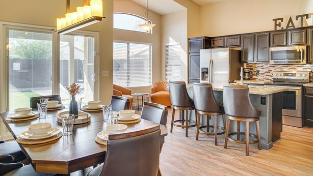 A modern kitchen with a dining area, featuring a large island, dark cabinetry, and a view of the backyard. - 2 Mi to Surprise Stadium! Snowbird Haven w/ Pool (Surprise)