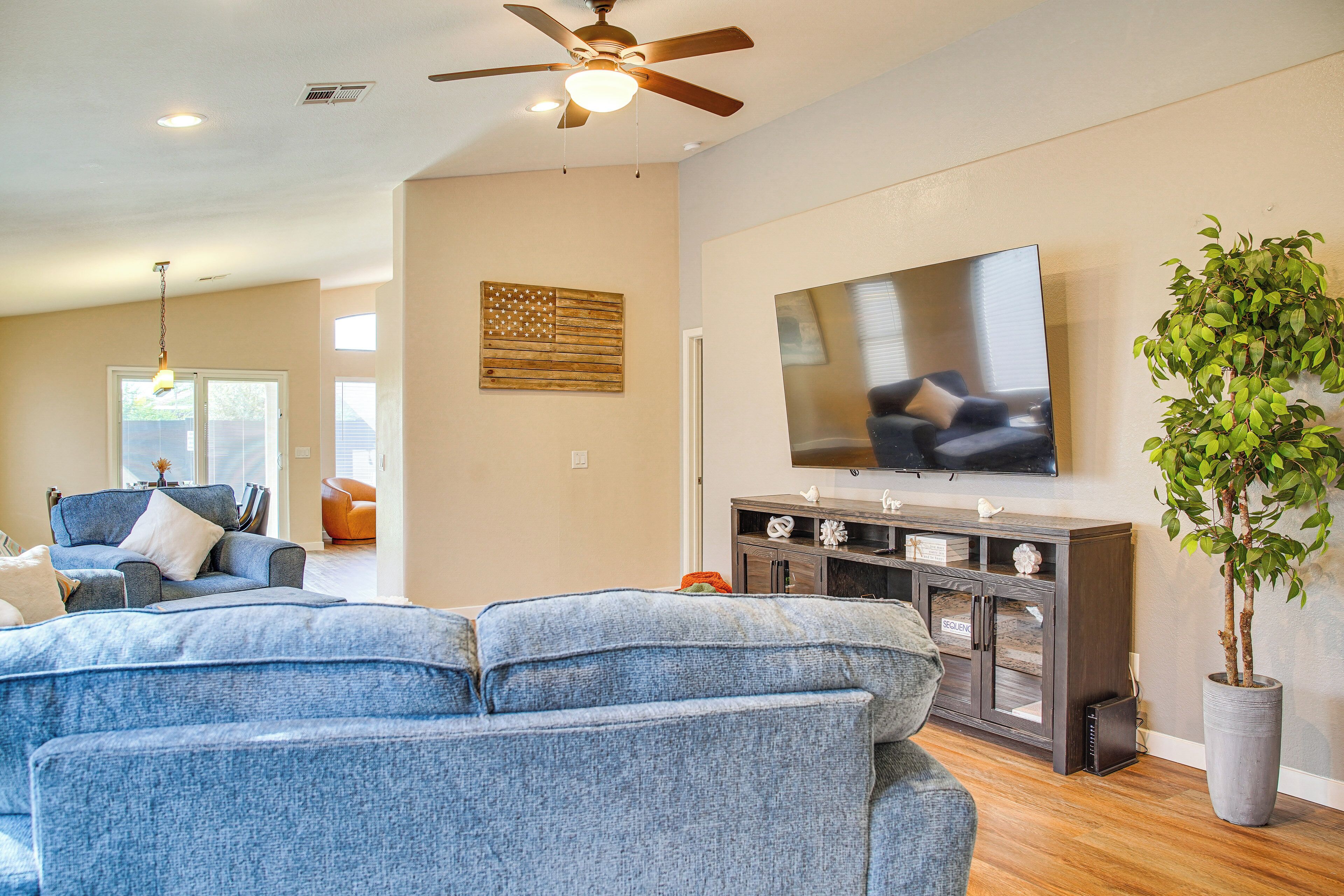 A living room with a large flat-screen TV, a ceiling fan, and a potted plant.
