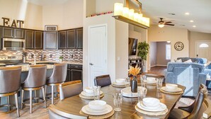 A modern kitchen with dark cabinets, a central island, and a dining area with a wooden table set for six. - 2 Mi to Surprise Stadium! Snowbird Haven w/ Pool (Surprise)
