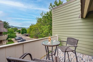 Un balcon avec des fauteuils en osier, une table en verre et une bouteille.