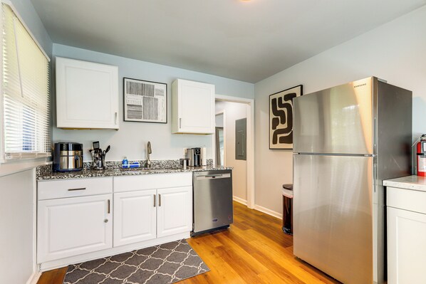 A modern kitchen with white cabinets, stainless steel appliances, and a wooden floor.