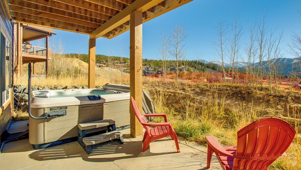 Un jacuzzi bajo una pérgola de madera con dos sillas rojas, con vistas a un paisaje montañoso.