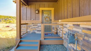 Fachada de madera con un muro de piedra, una reja metálica y un calentador de agua.