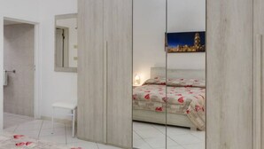 Una camera da letto con un letto, un comodino, una sedia, uno specchio e un quadro raffigurante un panorama urbano.