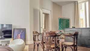 A dining area with a round table and wooden chairs, a television, and a framed picture on the wall.