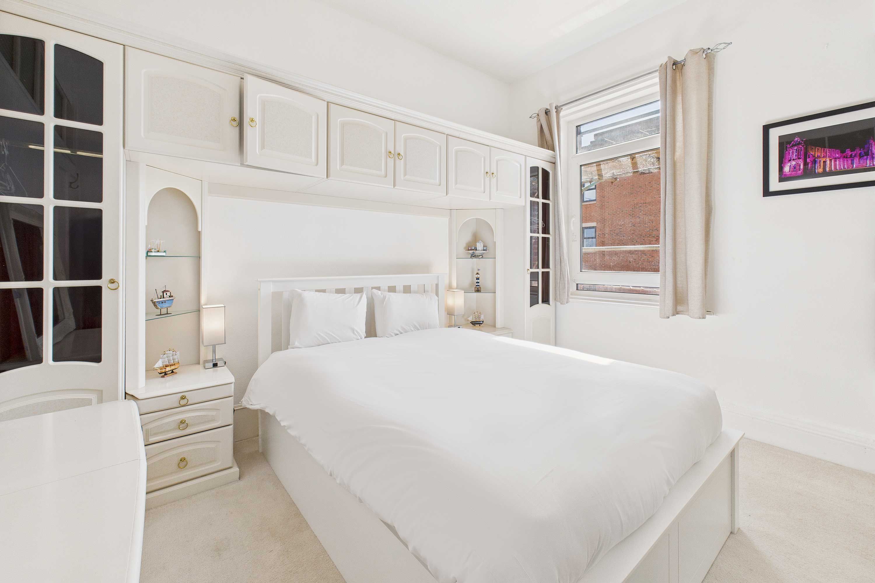 Une chambre à coucher avec un grand lit, une table de chevet, une commode et une fenêtre avec des rideaux.