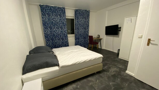 Ein Schlafzimmer mit einem Bett, einem Schreibtisch, einem Sessel und einem Fernseher.
