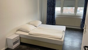 Ein kleines, sauberes Zimmer mit Bett, Heizkörper und einem fenster mit Vorhängen.
