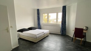 Ein Schlafzimmer mit einem Bett, einem Heizkörper, einem Fenster mit Vorhängen und einem Sessel.