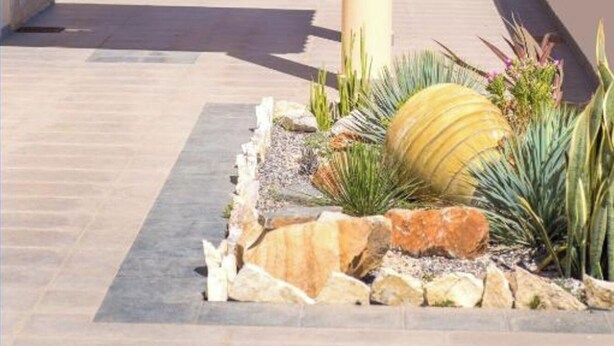 Una zona de pati amb una pèrgola, una taula amb cadires i un jardí rocall ornamental.