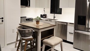 A modern kitchen with white cabinets, a stainless steel refrigerator, a microwave, and a stove. There is a wooden table with two chairs and a small stool. - Soleil & Sage Haven,2BR Townhouse in Cupecoy (Cupercoy)
